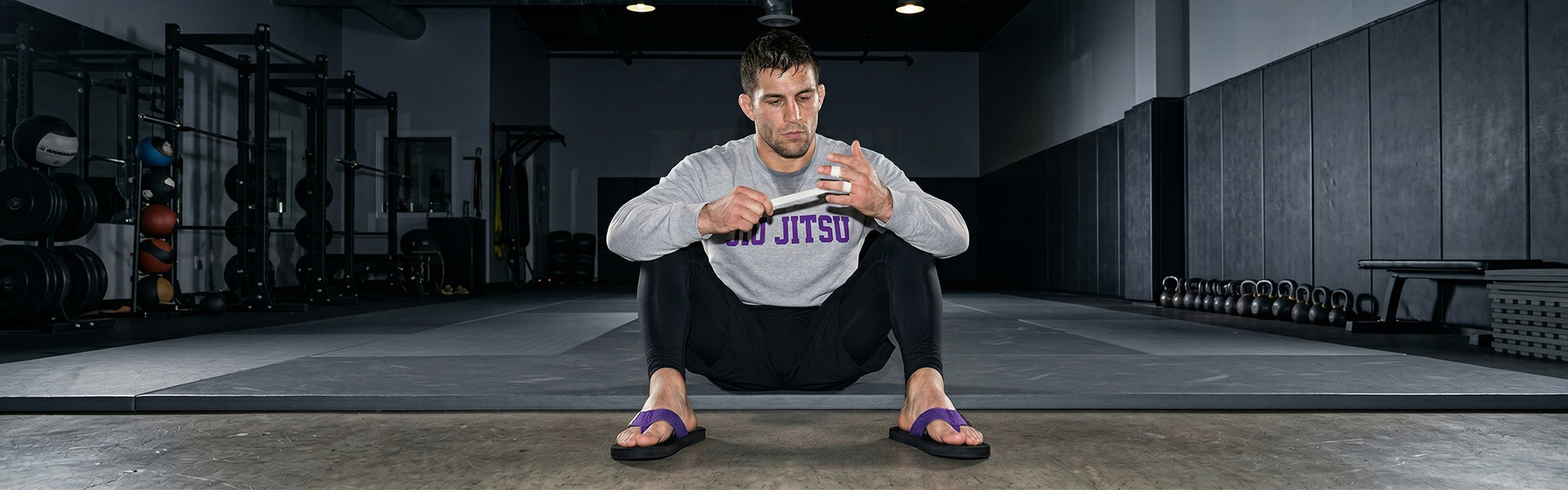 BJJ practitioner taping his fingers beside the mat while wearing purple belt flip flops