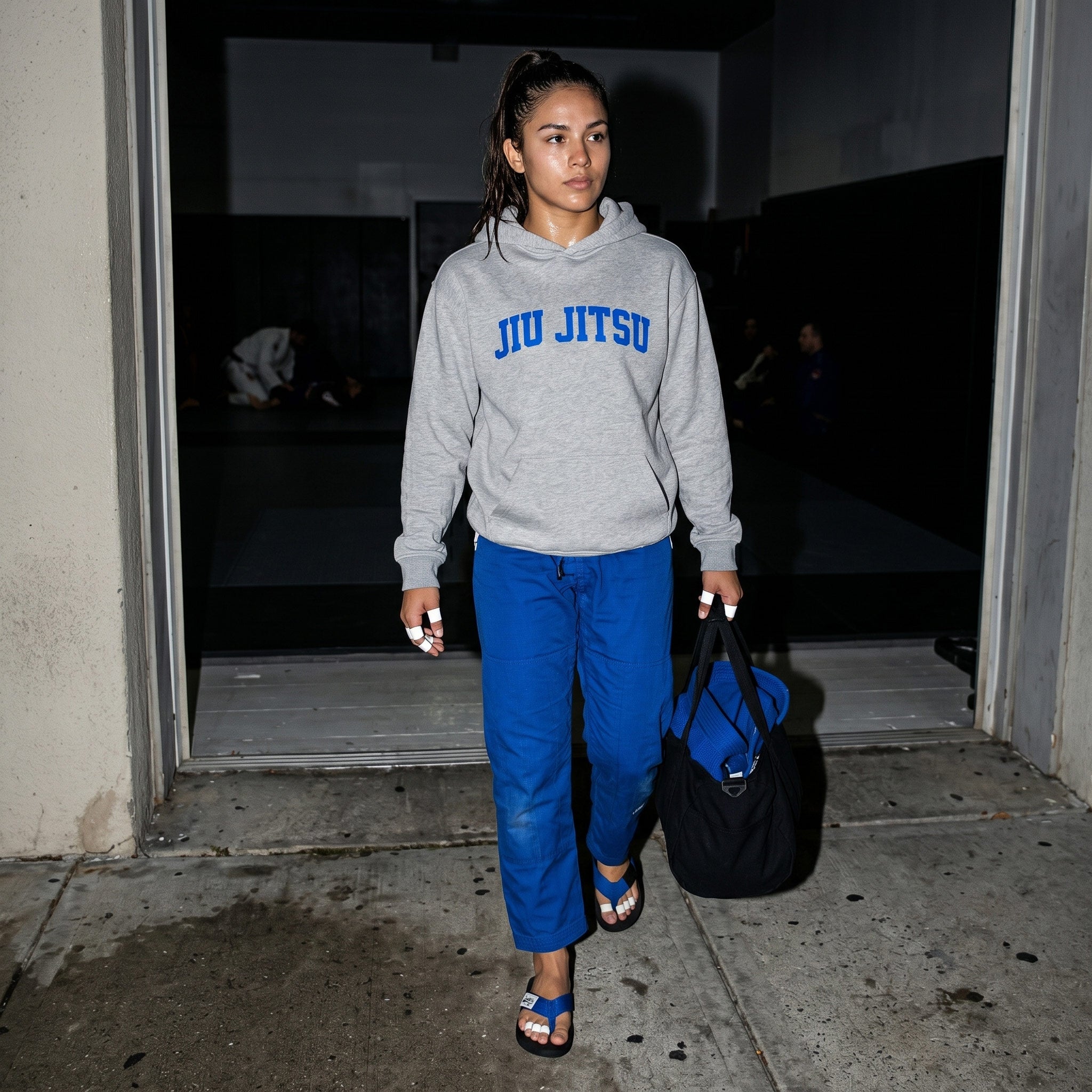 Female BJJ practitioner leaving the academy in blue Jiu Jitsu gear and blue belt flip flops