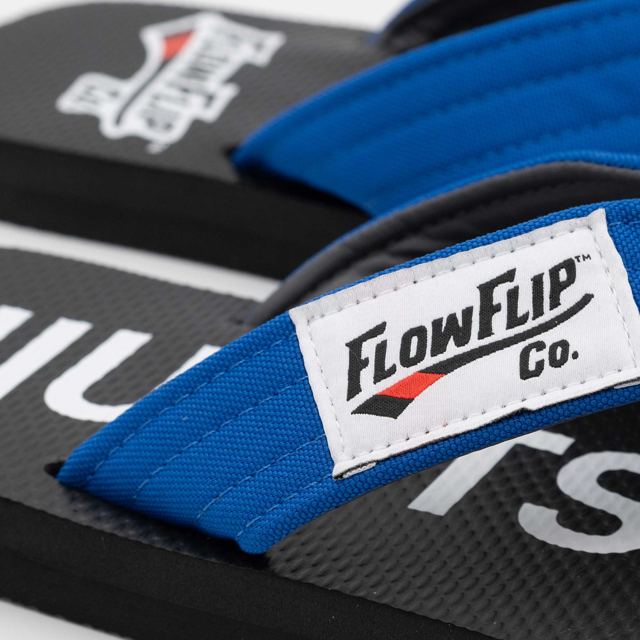 Close-up of the FlowFlip logo label on blue belt BJJ flip flops.