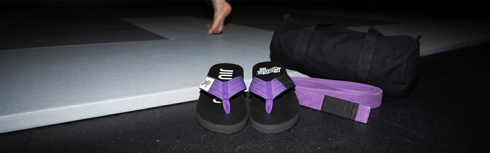 Purple belt BJJ flip flops, belt, and gym bag placed beside the mat before training