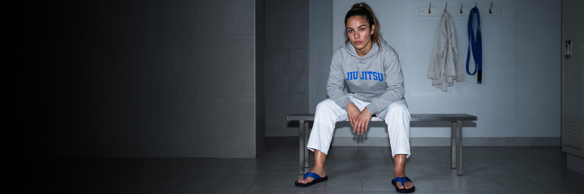 BJJ practitioner in blue belt flip flops seated in the changing area after training