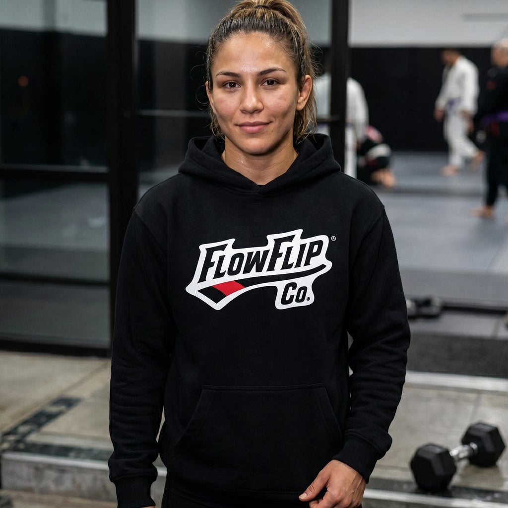 Black Jiu Jitsu hoodie worn in a BJJ academy setting with FlowFlip Co. chest logo visible.