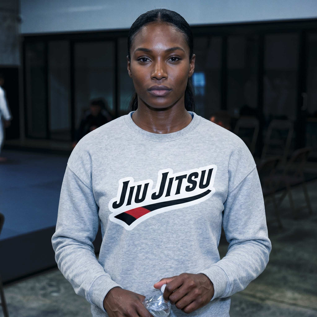 Grey Jiu Jitsu crewneck sweatshirt worn in a BJJ academy setting with chest artwork visible.