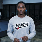 Grey Jiu Jitsu crewneck sweatshirt worn in a BJJ academy setting with chest artwork visible.