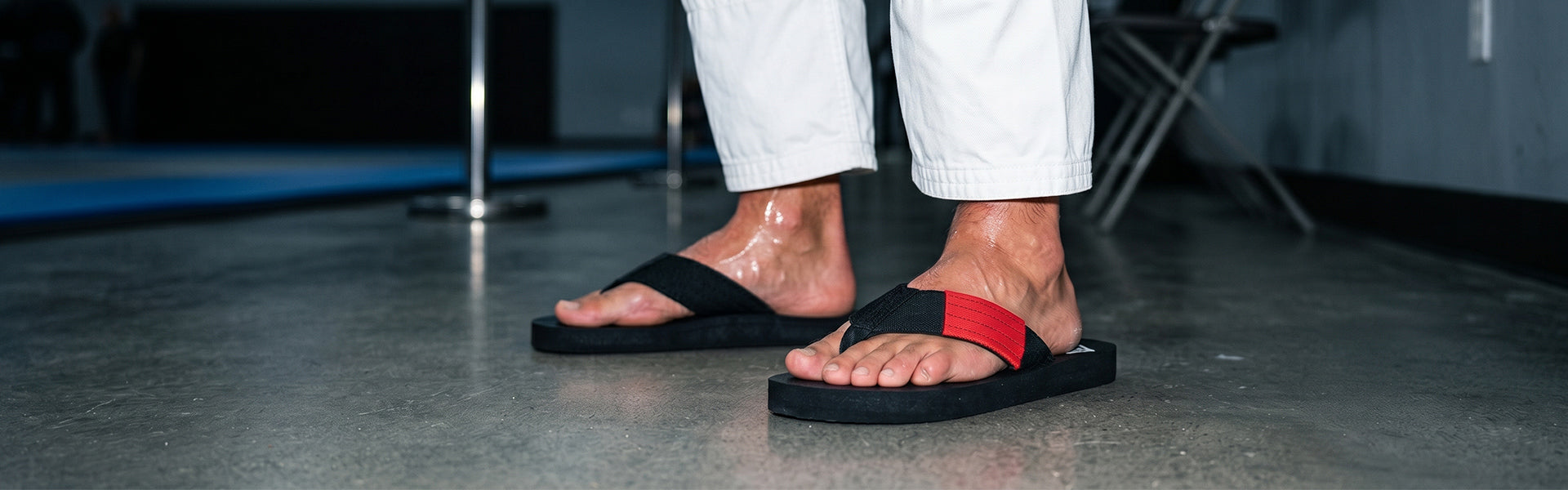 Close-up of black belt FlowFlip Co. BJJ  flip flops worn off the mat after training with white Jiu Jitsu gi pants