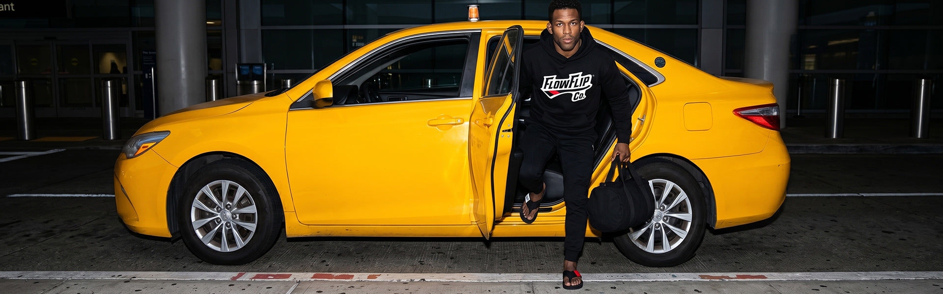 BJJ grappler in a FlowFlip Co. hoodie and black belt Jiu Jitsu flip flops stepping out of a taxi with a gym bag