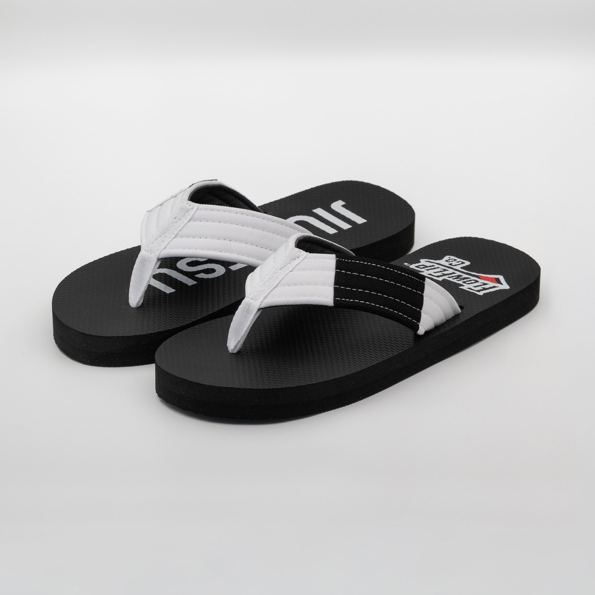 Angled pair view of adult white belt BJJ flip flops with white strap and black rank bar.
